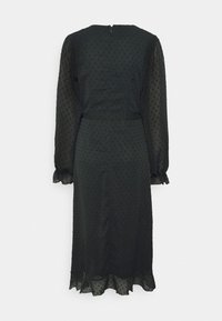 Vestido preto com bolinhas brancas, com mangas longas transparentes e decote redondo. Apresenta um cinto na cintura e uma bainha em camadas na parte inferior. Fecho na parte de trás com zíper.