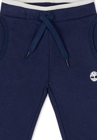 Donkerblauwe sweatpants met een zachte textuur, voorzien van een witte tailleband en trekkoord, zijzakken en een klein wit boompje logo.