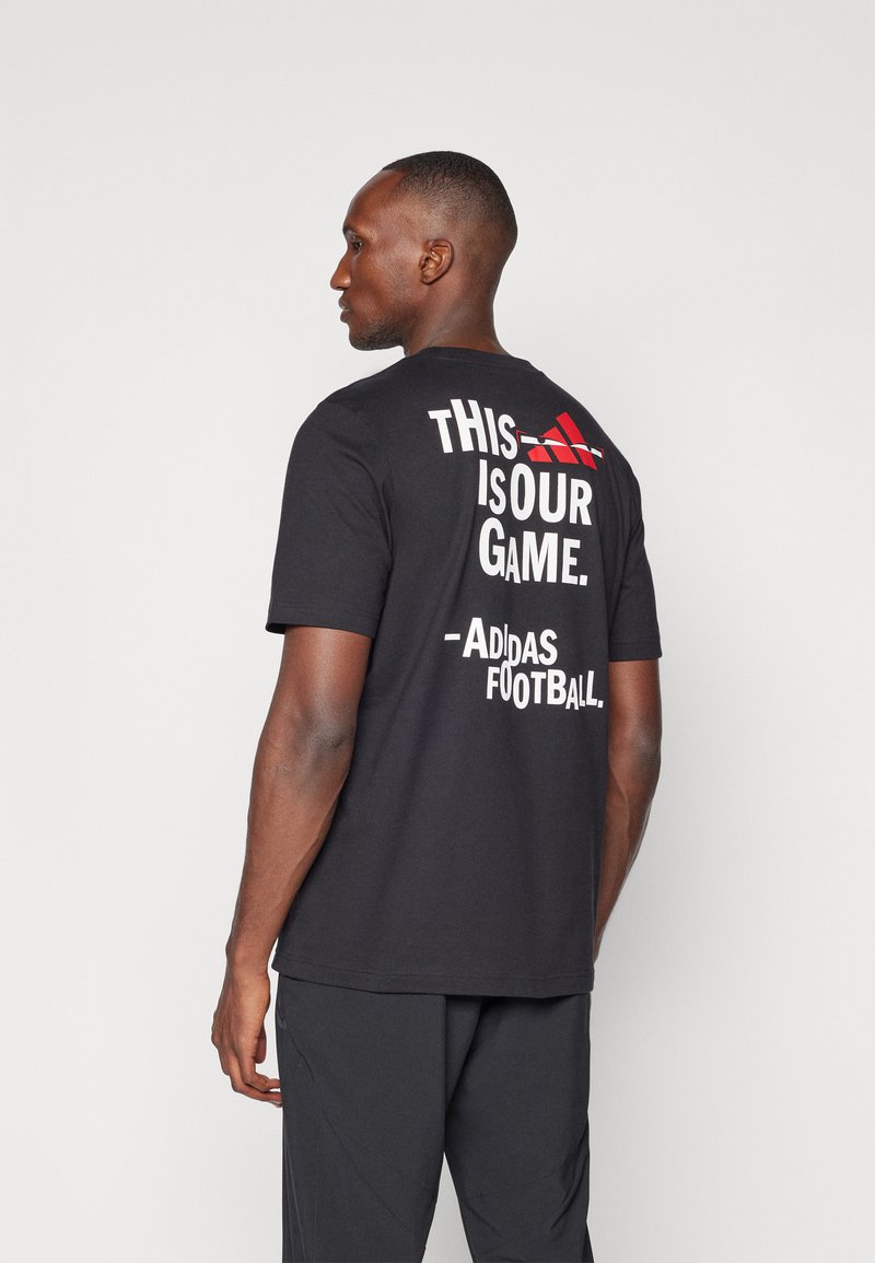 Sort bomulds T-shirt med korte ærmer, med hvid tekst og et rødt Adidas-logo på ryggen. Lige snit, minimalistisk design.