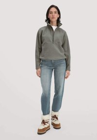 Fleece-Pullover in dezentem Grau mit einem halben Reißverschlusskragen, kombiniert mit hellblauen Jeans und braunen Stiefeln mit weißem Kunstfellbesatz.