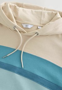 Sweat à capuche beige avec cordons réglables et blocs de couleur horizontaux en bleu clair et bleu sarcelle, taille medium avec étiquette de marque visible.