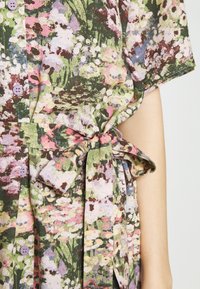 Robe à motif floral sur fond vert, ornée de fleurs roses et blanches. Tissu doux avec une taille ceinturée et des boutons violets.