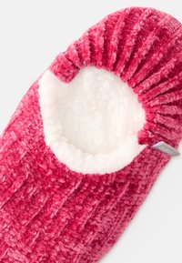Mjuk toffel i djup rosa, med ribbad utsida och mjukt vitt foder. Cirkulärt öppning för foten med en etikett på sidan.