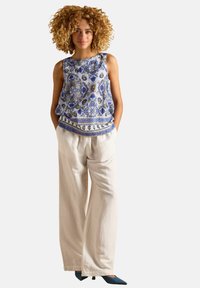 Sinise mustritega ilma varrukateta topp ümmarguse kaelusega, kombineeritud laiade valgete pükstega ja teal värvi terava ninaga kingadega.