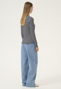 Maglietta a maniche lunghe a righe in blu navy e bianco, abbinata a jeans a gamba larga di un leggero blu chiaro con una sottile texture e tasche.