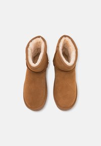 Brązowe zamszowe botki za kostkę z miękką kremową podszewką i zaokrąglonym czubkiem. Posiadają boczny szew oraz teksturowaną gumową podeszwę dla lepszej przyczepności.