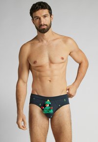 Męskie granatowe spodnie z pluszowymi zielonymi wzorami bałwanka i drzewa. Charakteryzują się gładką fakturą i dopasowanym krojem oraz wielokolorowymi ozdobnymi akcentami.