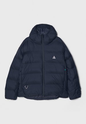 Navy puffer jacket with a zippered front, hood, and padded design. Features a triangular logo on the chest and a unique accent on the hem.
