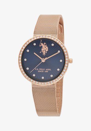 Orologio in oro rosa con cinturino in maglia, caratterizzato da un quadrante blu navy, accenti in cristallo e un logo di giocatore di polo. Cassa rotonda, lucida, con motivo radiale.