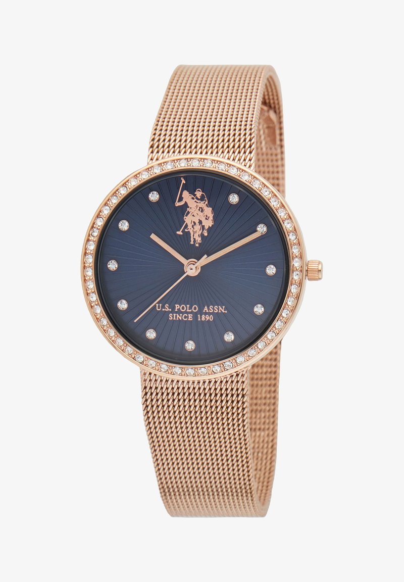 Orologio in oro rosa con cinturino in maglia, caratterizzato da un quadrante blu navy, accenti in cristallo e un logo di giocatore di polo. Cassa rotonda, lucida, con motivo radiale.