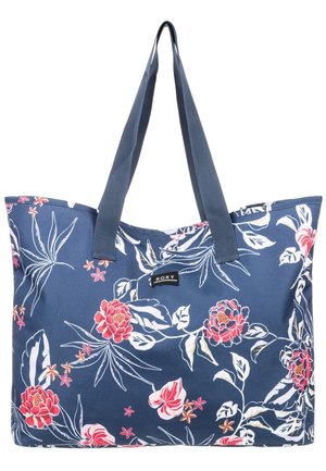 Blauwe tote tas met donkerblauwe handvatten, versierd met witte en roze bloemenpatronen en een klein zwart "Roxy" logo-label aan de voorkant.