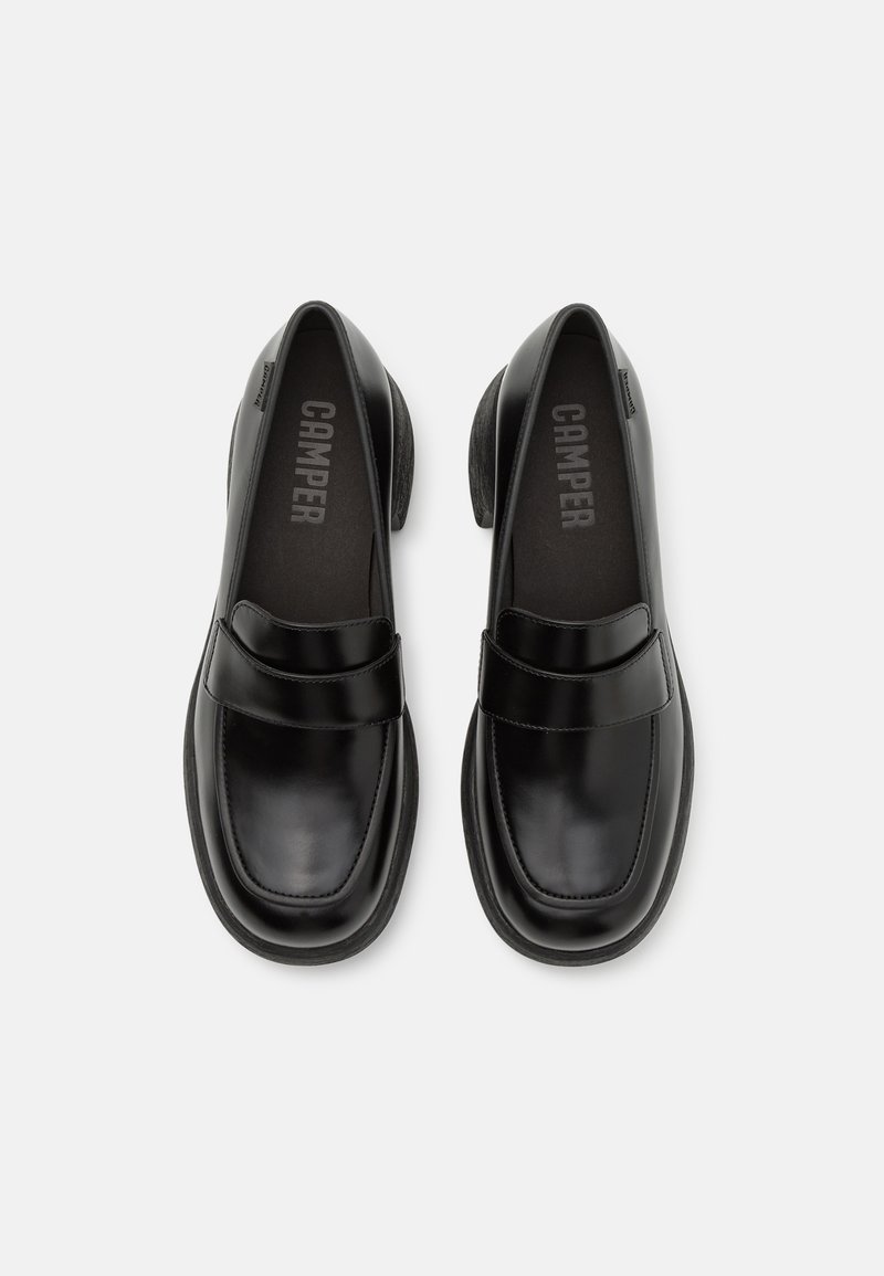 Mocassins en cuir noir avec une finition lisse, présentant des détails cousus sur le dessus et un talon bas. Nom de la marque visible à l'intérieur.
