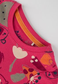 Rosa Baumwollhemd mit bunten Tier- und Blumenmotiven. Mit orangenem Kragen und zwei Druckknöpfen an der Schulter für einfaches An- und Ausziehen.