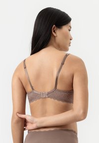 Spetsrygg-bh i en dämpad brun färg med justerbara band och krok-och-öga-stängning. Har vågiga kanter och intrikata mönster.