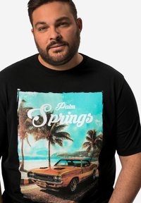 Černé tričko s barevným potiskem klasického oranžového auta s palmami a plážemi, nad obrázkem je nápis "Palm Springs".