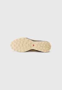 Shoe sole with a textured, rubber material; features a tread pattern with pronounced lugs and a midsole in beige with a red triangular accent.