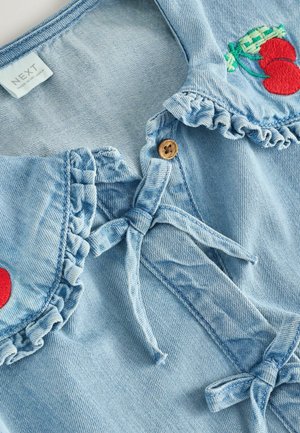 Hellblaues Denim-Oberteil mit Rüschensaum, Holzknopf und Kirschstickerei. Weicher Stoff mit Bindebändern.