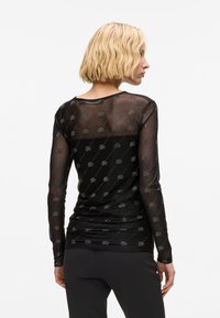 Schwarzes Langarmshirt aus transparentem Stoff mit einem Rautenmuster und metallischen Akzenten. Glatte Textur mit einer körpernahen Silhouette.