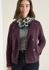 Burgundy, textured double-breasted jacket with two large buttons, paired with a gray sweater and patterned scarf featuring black, white, and mint colors.