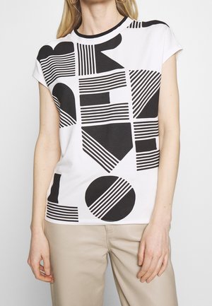 Weißes T-Shirt mit schwarzen geometrischen Mustern, darunter Linien und Formen. Kurze Ärmel und Rundhalsausschnitt. Kombiniert mit hellbeigen Hosen.