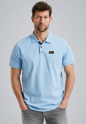 Hellblaues Poloshirt mit Kragen, Drei-Knopf-Leiste und kleinem schwarzem und goldenen Logo-Patch auf der linken Brust. Baumwollmaterial, kurze Ärmel.