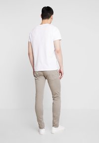 Camiseta blanca de manga corta combinada con pantalones slim-fit beige claro, con bolsillos traseros y zapatillas blancas. Fondo neutro.