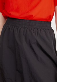 Svart elastisk midjeskirt gjort av lättviktig tyg, med en samlad textur och flödande design. Kombinerad med en röd topp.