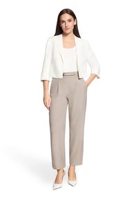 Blazer blanc sur mesure avec manches trois-quarts, associé à un pantalon beige taille haute et des escarpins blancs à bout pointu.