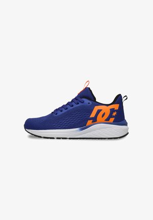 Niebieski sportowy sneaker z pomarańczowym logo z boku, biała podeszwa z czarnym bieżnikiem i pomarańczową pętlą na języku i pięcie.