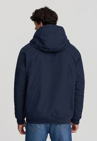 Giacca con cappuccio blu navy con chiusura a zip, polsini a costine e una texture liscia, con un design leggermente imbottito per il calore.