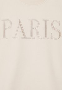 Felpa crema con la scritta "PARIS" in lettere embossate di un beige chiaro. Tessuto morbido con collo a girocollo a coste.
