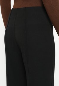 Čierne priliehavé nohavice z hladkej látky s viditeľnými švami a vysokým pásom, skombinované s hnedým rebrovaným topom.