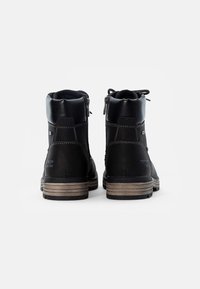 Botas de tobillo de cuero negro con acabado texturizado, que presentan un cierre lateral con cremallera, detalles de costura y una suela de goma marrón en capas.