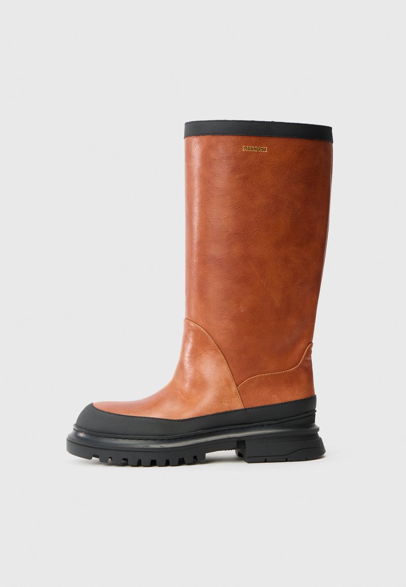 Bota castanha de couro até ao joelho com sola de borracha preta e borda superior. Textura suave com um leve brilho e detalhe de design curvado.