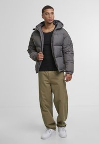 Grå puffjakke med hette, med glidelås og quiltet design; kombinert med olivengrønne vide bukser og hvite joggesko.