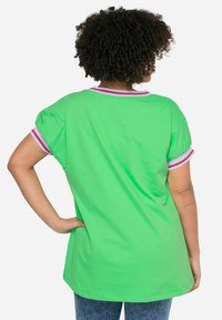 Grøn bomulds t-shirt med korte ærmer og rund halsudskæring. Har pink og hvide stribede detaljer på halsudskæringen og ærmerne.