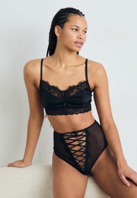 Svart sateng-bralette med blondekant og matchende høytlivsundertøy med gjennomsiktig mesh-front og kryssbånd-detall.