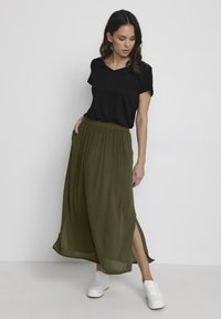 Black short-sleeve v-neck top paired with an olive green, ankle-length skirt featuring a gathered waistband and side slits, complemented by white sneakers.