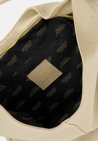Beżowa skórzana torebka z czarnym wykończeniem wnętrza, na którym widnieje napis "Venezia Made in Italy", oraz wewnętrzną kieszenią na zamek.