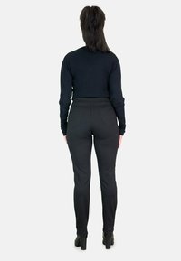 Pantalones negros ajustados con un patrón texturizado, bolsillos traseros y un diseño de tiro medio, combinados con una blusa negra de manga larga. Botas negras de tacón alto.