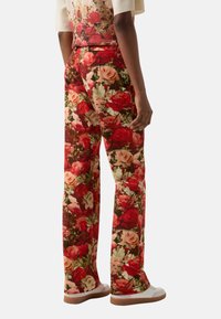 Floral trousers featuring a vibrant print of red and pink roses on a dark background, straight leg design, and smooth fabric texture.