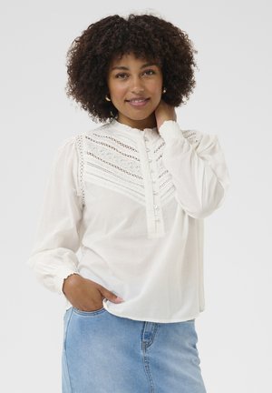 Witte blouse met ingewikkelde kantdetails, knoopsluiting aan de voorkant en geplooide manchetten. Gecombineerd met een lichtblauwe denim rok.