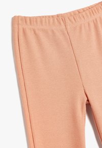 Nærbillede af ferskenfarvede ribbet stof leggings med elastisk talje og lodrette sømdetaljer på hvid baggrund.