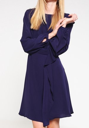 Robe bleu marine de longueur genou avec des manches longues, détail froncé à l'épaule et coupe ample, fabriquée à partir d'un tissu léger et lisse.