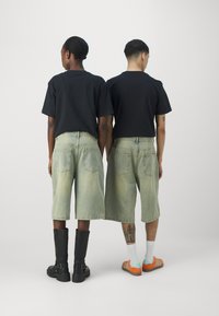 T-shirts noirs, shorts en denim kaki avec de grandes poches arrière, et des chaussures contrastantes : bottes noires et baskets orange avec des chaussettes blanches.