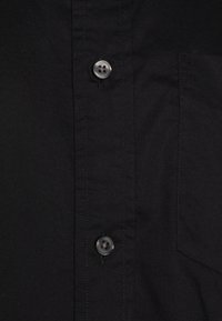 Gros plan sur un tissu de chemise noir avec deux boutons noirs et une partie d'une poche cousue sur le côté droit.