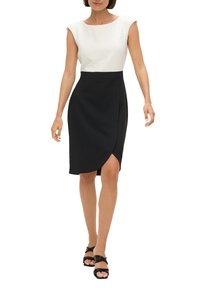 Robe avec un haut blanc et une jupe portefeuille noire, présentant une coupe au genou et des manches courtes. Tissu lisse avec un léger éclat.