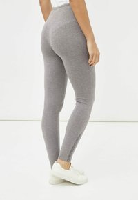 Leggings grises hechos de una tela suave, con un diseño ajustado y una cintura alta, con botones laterales en el dobladillo, combinados con zapatillas blancas.