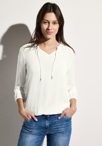 Lichte witte blouse met een V-hals, een trekkoordcapuchon en driekwart mouwen, gecombineerd met blauwe denim jeans. Soepele stoftextuur.