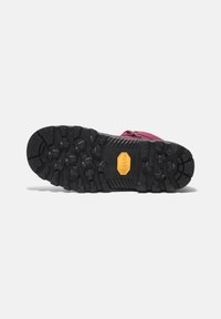 Semelle extérieure en caoutchouc noir avec un profond relief, arborant un logo Vibram jaune. La tige présente une couleur bordeaux avec une fermeture éclair.